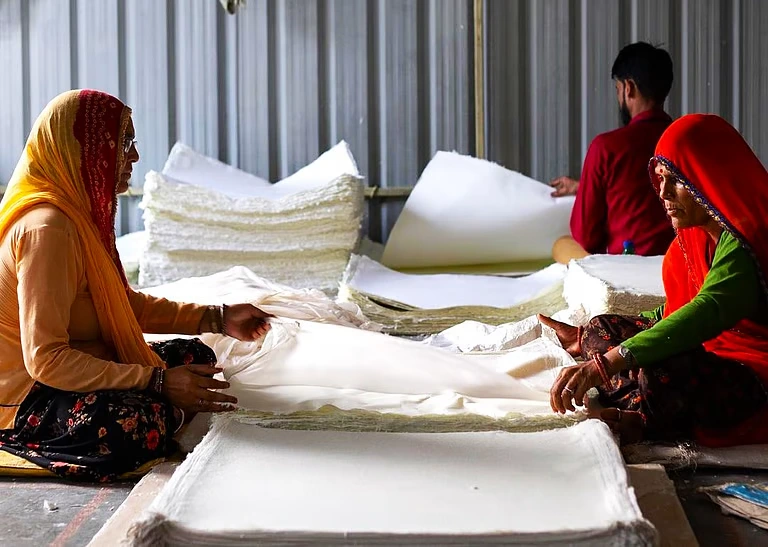 The image features three artisans in a workshop setting, engaged in the production of handmade paper.