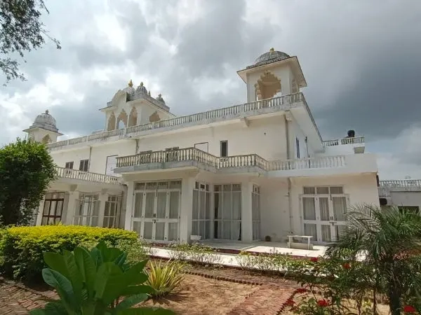 A white building of Savista Retreat with traditional architecture and domes, surrounded by greenery under a cloudy sky.