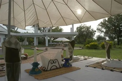 A close-up of an outdoor dining table setup at the Savista Retreat. The table is covered with white linen, featuring elegant place settings with candles, napkins, and woven mats.