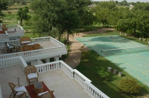 This wide, high-angle shot showcases a portion of the Savista Retreat in Jaipur, Rajasthan. Balconies overlooking tennis court and scenic Rajasthan landscape.