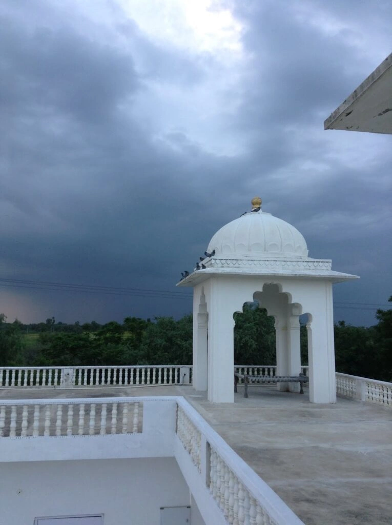 White domed rooftop with a cloudy sky, offering a peaceful view of the surrounding greenery and balcony railing.