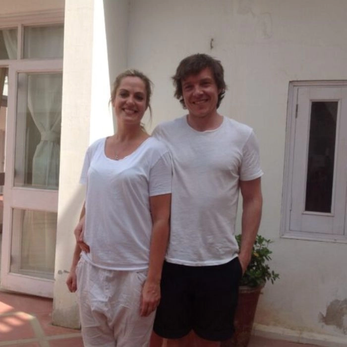 Smiling pair in white outfits posing in the courtyard of a building, creating a warm and welcoming outdoor scene