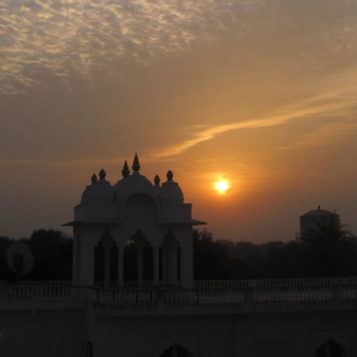 A beautiful sunset with a clear sky behind a white architectural structure, likely a temple or palace, with the sun setting behind.