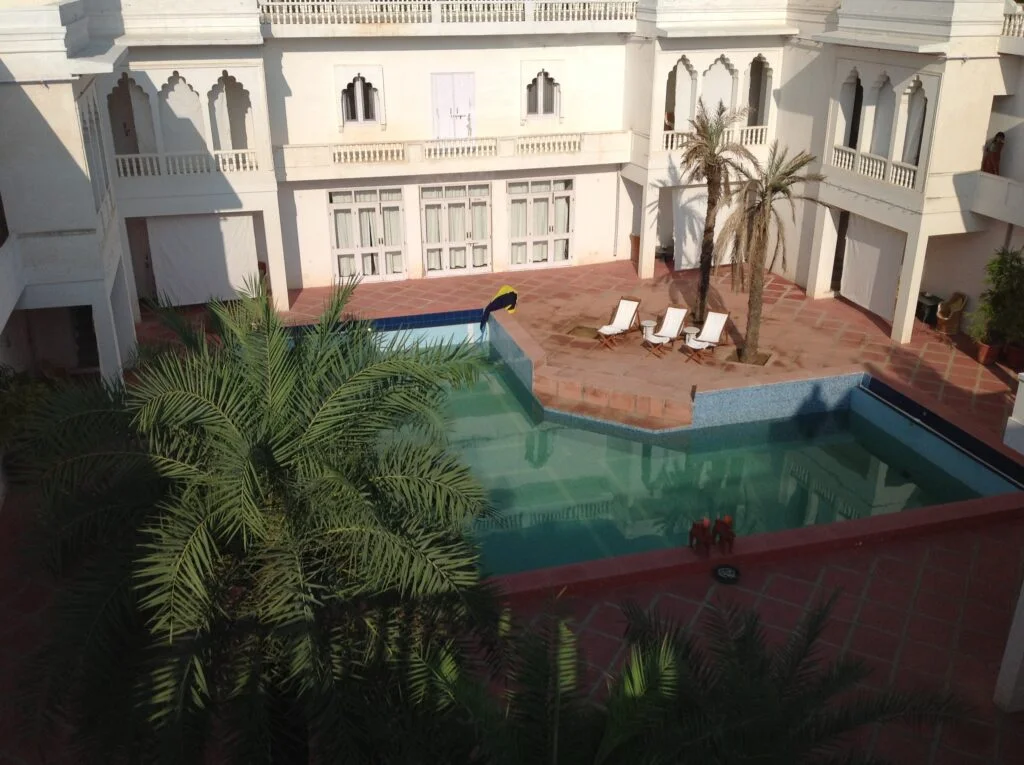An eye-level shot shows the resort's open-air concept with its outdoor swimming pool encompassed by sun chairs, trees and the rooms looking down upon it.