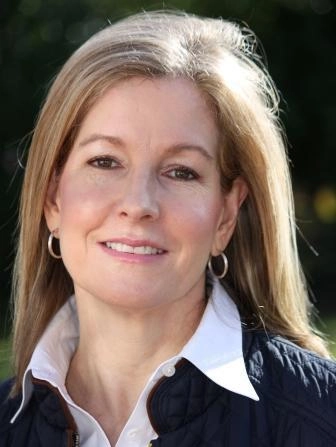 Woman with blonde hair, smiling with silver hoop earrings.