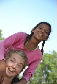 Smiling woman guest at Savista Retreat carries a local girl on her back under a clear sky, sharing a playful outdoor moment