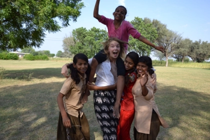 A group of girls, including one guest of Savista Retreat, smiling and playing in an outdoor grassy area with trees in the background