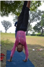 A portrait shot of a young girl stands upside down with her hands positioned on a small flat blue mat.