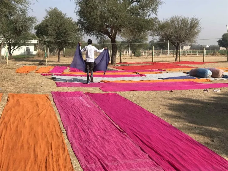 At Savista Retreat, a man spreads out dyed fabrics horizontally on the ground to dry in the sun.