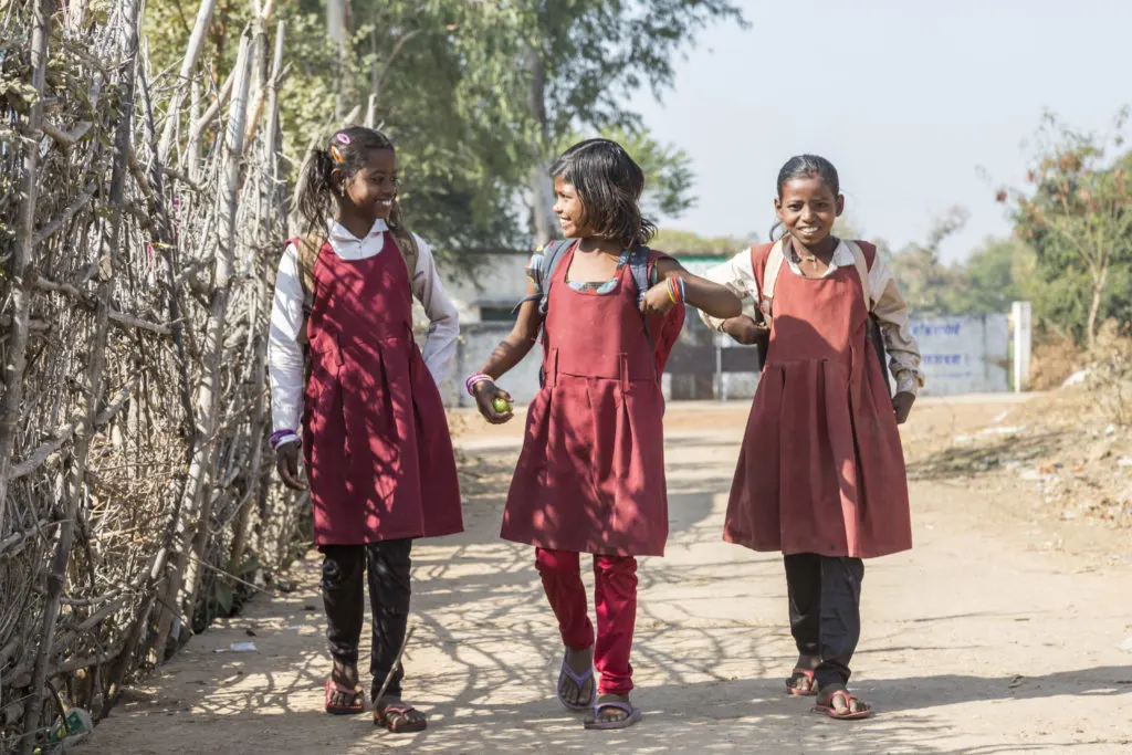 Happy and young schoolgirls in uniforms walking hand in hand down a rural path, smiling joyfully in a peaceful countryside setting
