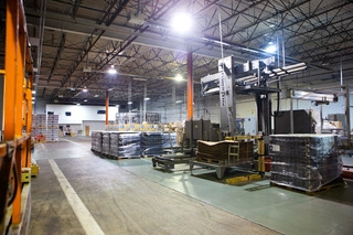 Interior of a warehouse with stacked pallets and industrial equipment under bright lighting.