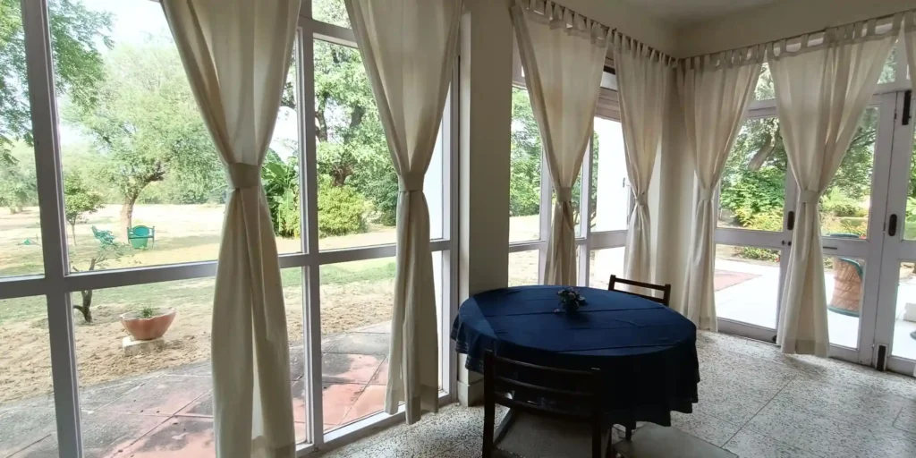 A dining area with a table set with a blue tablecloth, chairs, and a view through large windows.