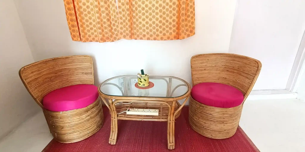 A close-up of a small coffee table with two wicker chairs, a decorative item on the table, and a window with orange curtains.