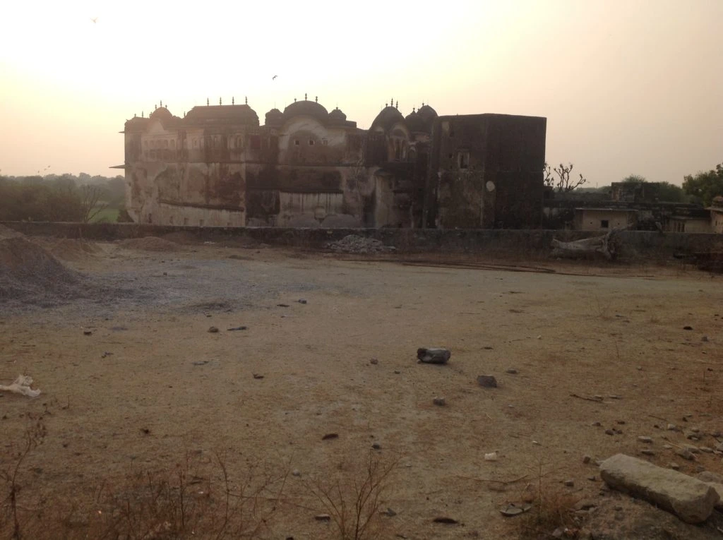 An old, weathered fort or palace building on the way of Sambhar Lake with crumbling walls, situated in a dry, barren landscape under a setting sun