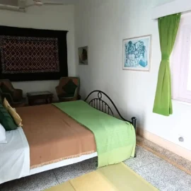 A bedroom featuring green curtains, a bed with brown and green bedding, a wooden desk, and a seating area.