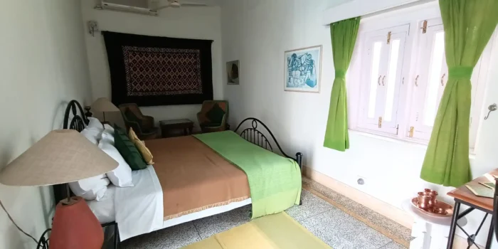 A bedroom featuring green curtains, a bed with brown and green bedding, a wooden desk, and a seating area.