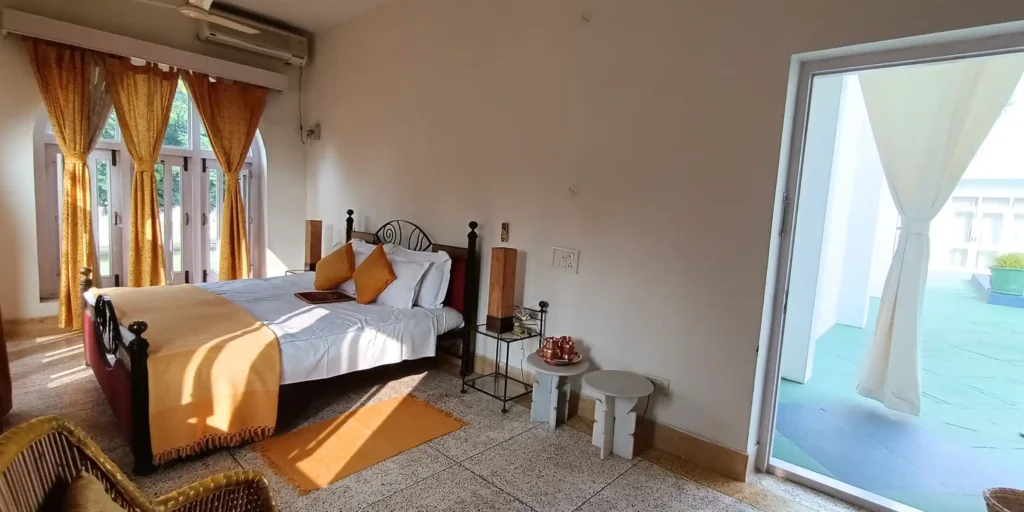A bedroom with yellow curtains, a bed with yellow and white linens, and an open door leading to a balcony with a view.
