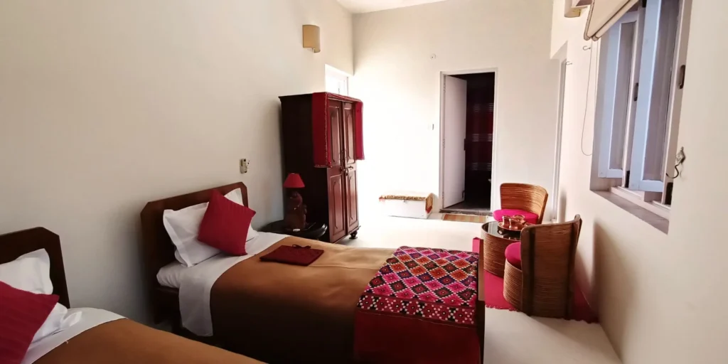 A cozy sitting area in the bedroom featuring wicker chairs with bright cushions and a glass table.