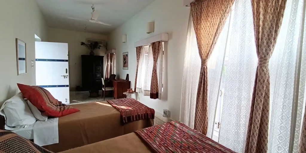 A close-up view of the bedroom with focus on curtains, light streaming through the window, and the decorative patterns on the bed covers.