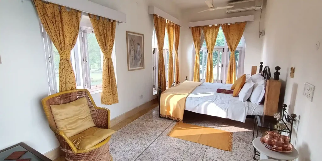 A bedroom with yellow curtains, a bed, a chair with yellow cushions, and decorative items on a side table.