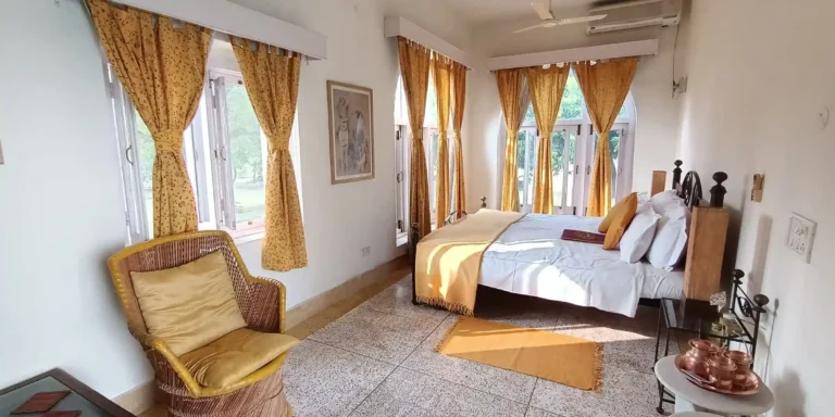 A bedroom with yellow curtains, a bed, a chair with yellow cushions, and decorative items on a side table.