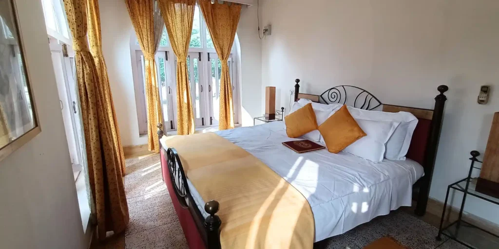 A bedroom with yellow curtains, a bed adorned with yellow and white pillows, and a wooden table with a book placed on it.