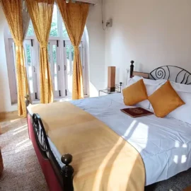 A bedroom with yellow curtains, a bed adorned with yellow and white pillows, and a wooden table with a book placed on it.