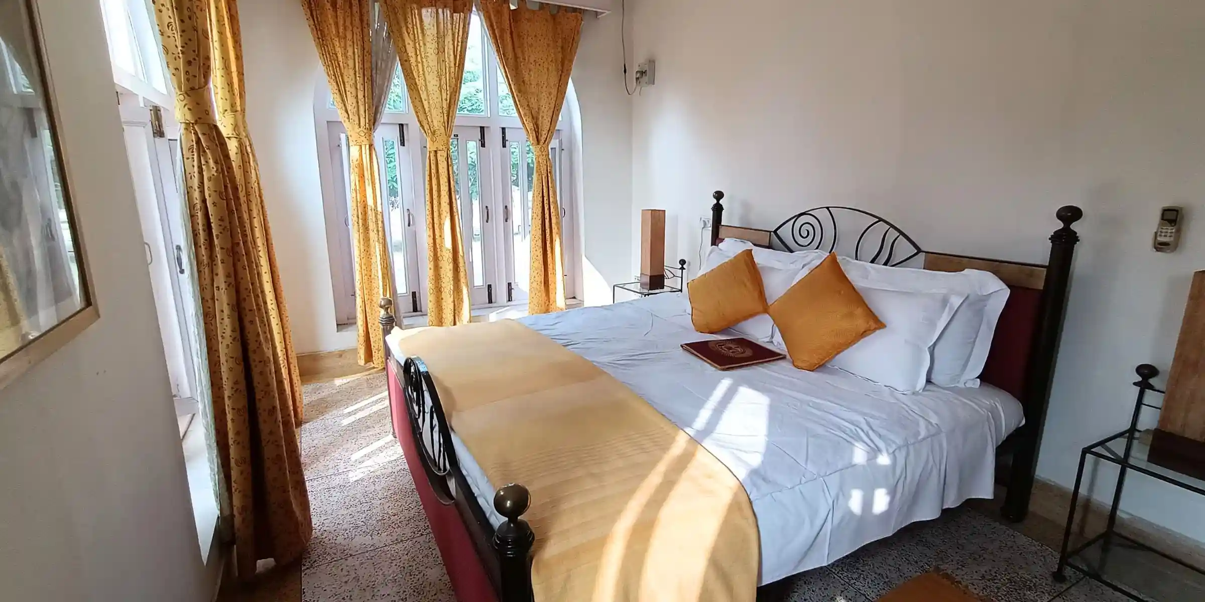A bedroom with yellow curtains, a bed adorned with yellow and white pillows, and a wooden table with a book placed on it.