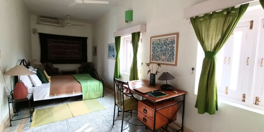 A bedroom with green curtains, a bed with brown and green bedding, and artistic wall hangings.