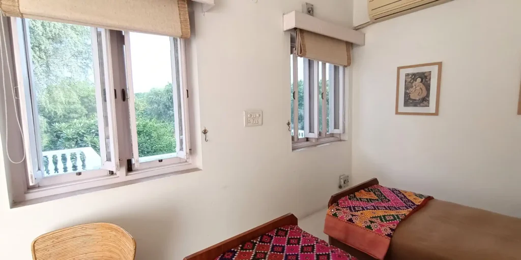 View of the bedroom with open windows, showcasing vibrant artwork on the wall and patterned bedspreads.