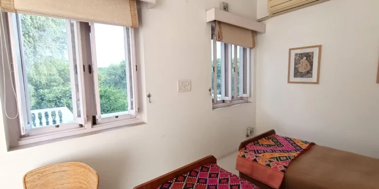 View of the bedroom with open windows, showcasing vibrant artwork on the wall and patterned bedspreads.