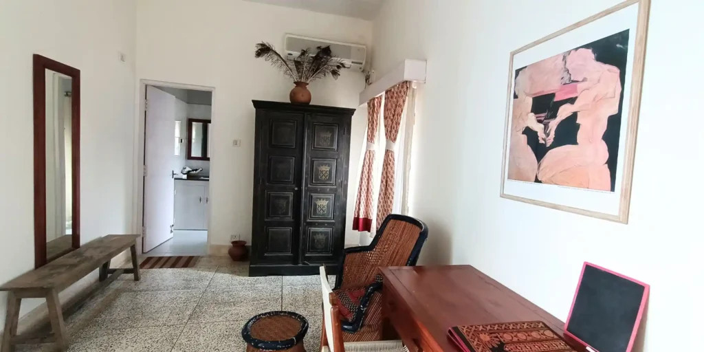 Another view of the bedroom showing a wooden table, an artwork on the wall, and decorative curtains.
