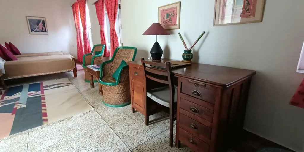 A room featuring a desk, wicker chairs, decorative items on the table, and red curtains.