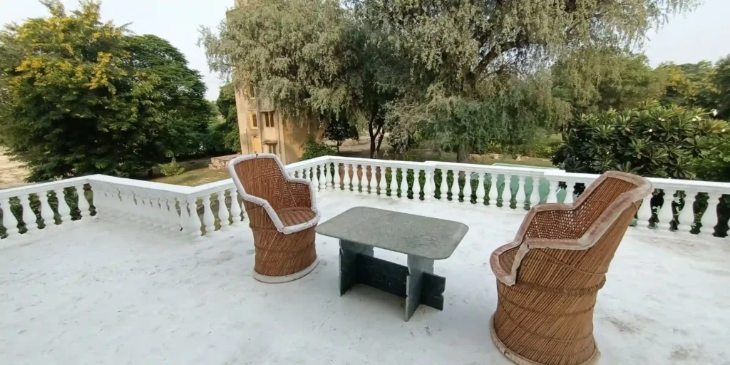 A terrace with two wicker chairs and a stone table overlooking a lush garden area.