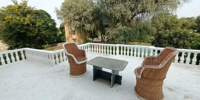 A terrace with two wicker chairs and a stone table overlooking a lush garden area.