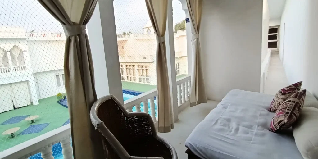 "Cozy balcony with wicker chair, cushions, and view of courtyard with pool