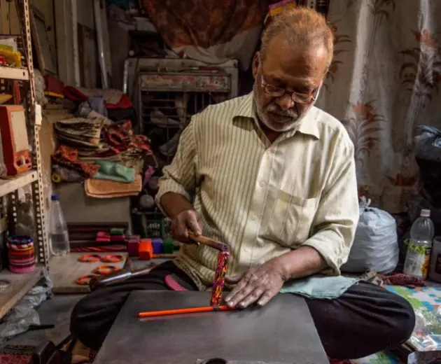 A man painting an bangle in his workshop with bright colors, using traditional methods.