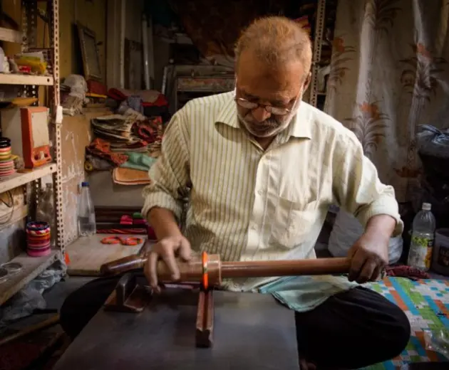 A man shaping a colorful bangle on a metal surface with tools in a small workshop.