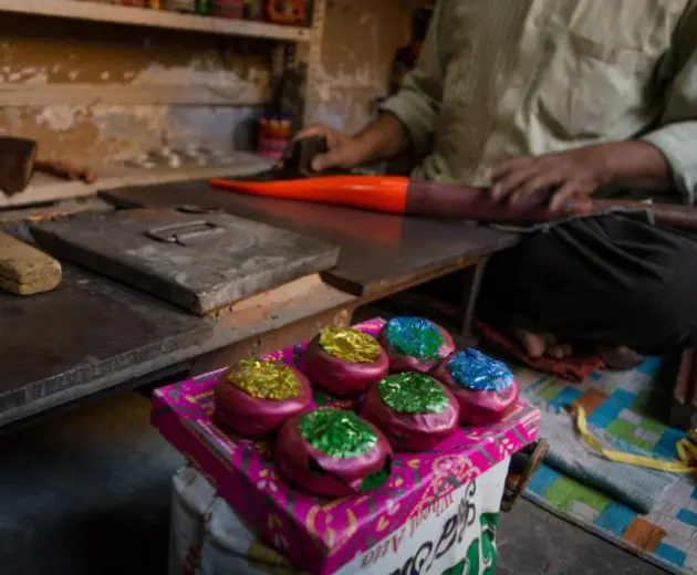 A man handcrafting items in a workshop, surrounded by brightly colored materials.