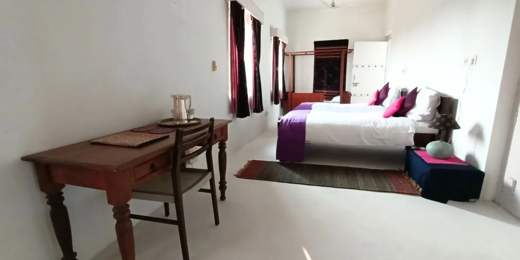 Neat bedroom with two single beds, purple and pink accents, and wooden furniture