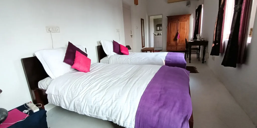 Bright bedroom with two single beds, purple accents, and wooden furniture