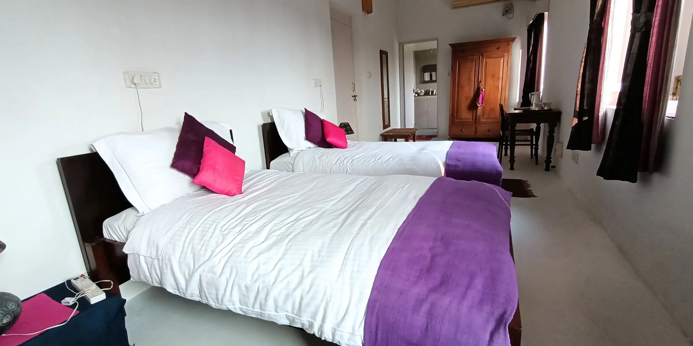 Bright bedroom with two single beds, purple accents, and wooden furniture