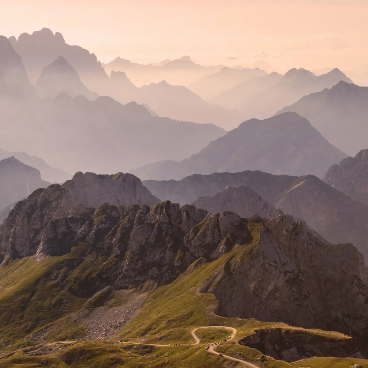 A scenic view of mountains and winding roads with a misty atmosphere during sunset