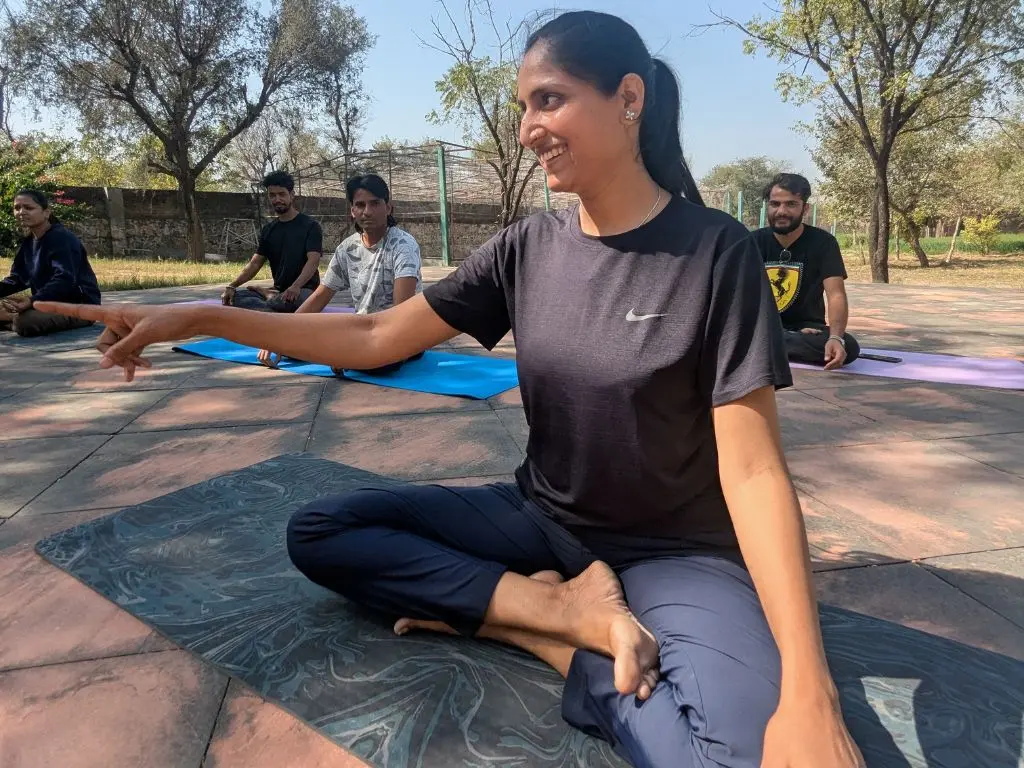 Smiling woman pointing during an outdoor yoga session with others in a open space.