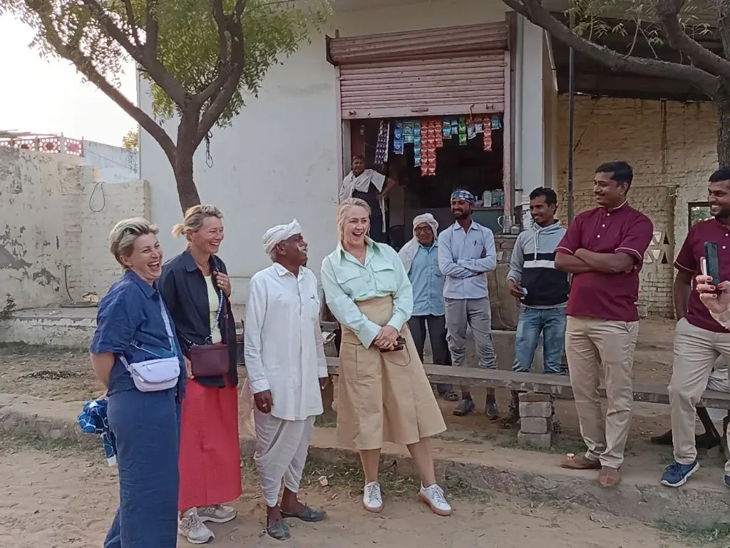 Group of people smiling and interacting outdoors, with locals and tourists gathered together in a community setting.