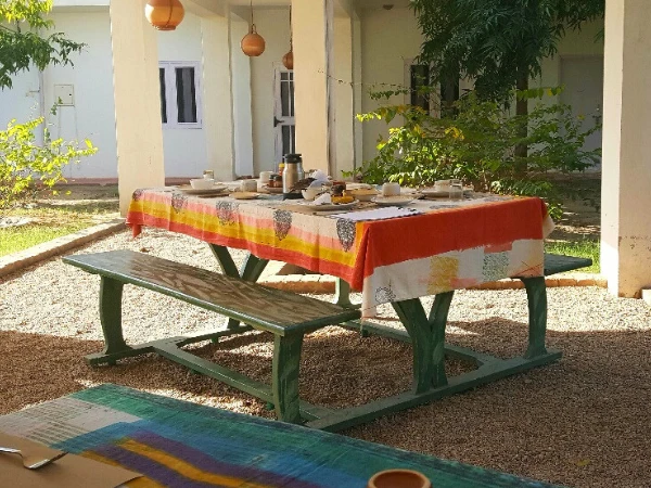 An outdoor picnic table set for a meal under a covered patio in a garden courtyard.
