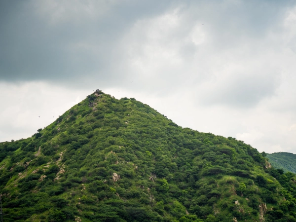Lush green mountain peak beneath a cloudy, overcast sky during the Rajasthan monsoon.