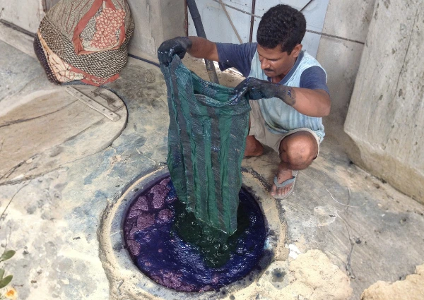 Fabric stamped with dark clay mud-resist patterns being lifted from a natural blue indigo dye vat, demonstrating the traditional Dabu printing technique.