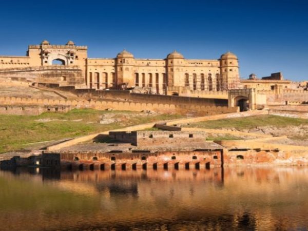The majestic Amber Fort in Jaipur, Rajasthan, rising against a clear blue sky, with its beautiful architecture reflected in the calm waters below.