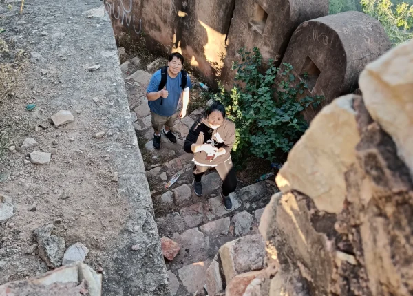 Two tourists climb stone steps at Jaigarh Fort, Jaipur, with arched walls and greenery in the background.